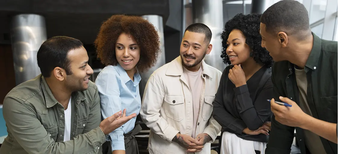 Group of five colleagues engaged in conversation, standing together and smiling.