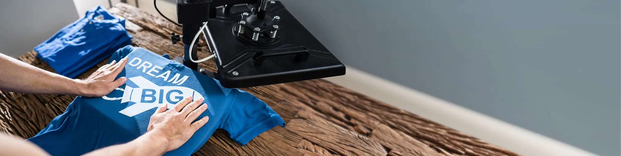 Close-up of a heat press machine pressing a blue T-shirt with the words 'Dream Big' printed on it.