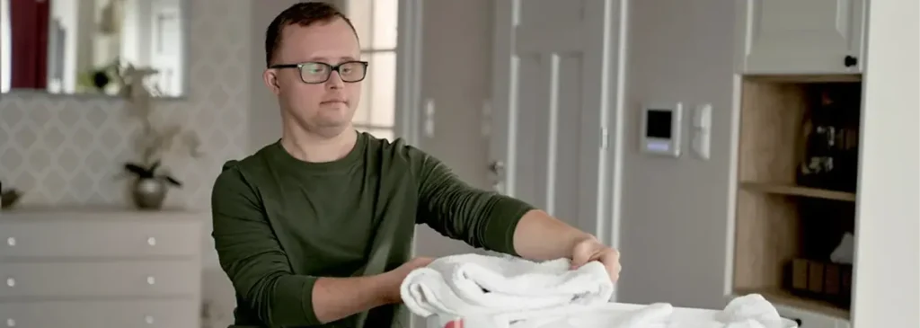 Man folding freshly washed white towels in a modern kitchen with a calm expression.