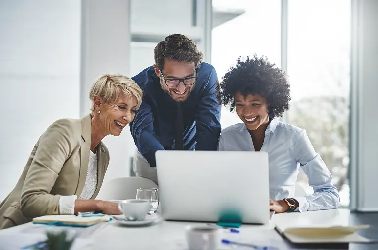 Three business colleagues smiling and looking at a laptop together.