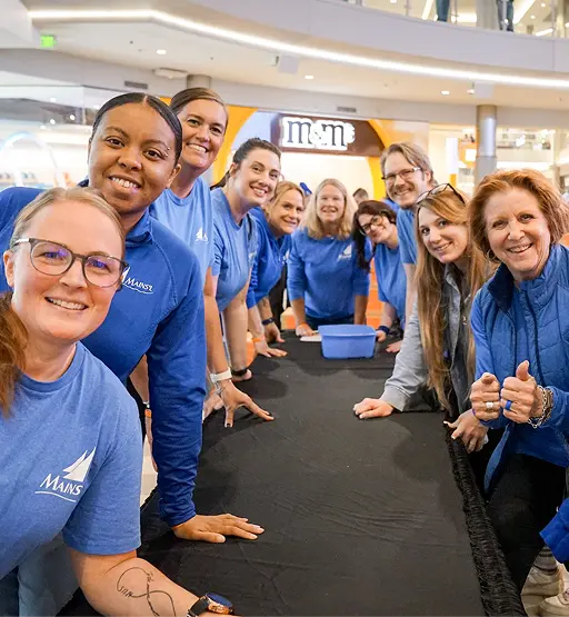Group of smiling Mains’l team members wearing blue shirts gathered around a table at a Matterbox event.