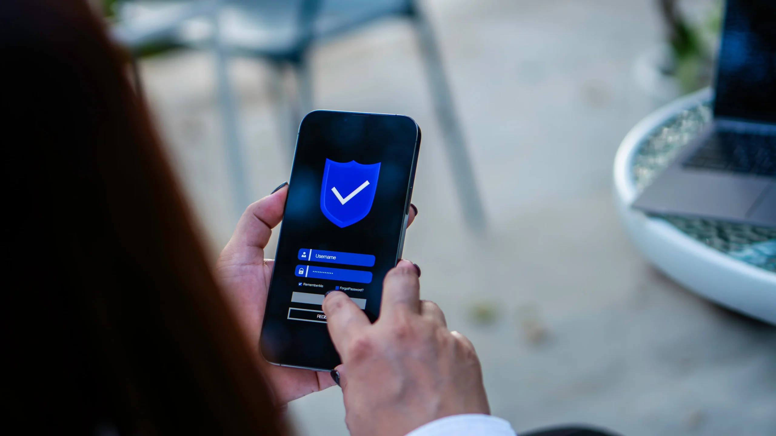 Person using a smartphone with a security app open, showing a shield icon and login fields, verifying or signing in.