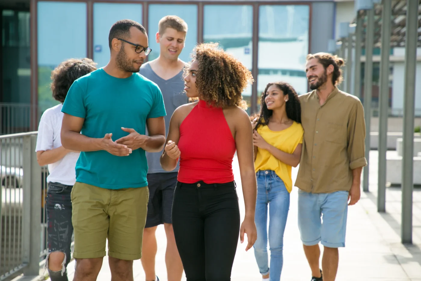 group-of-people-walking-talking-smiling Group of diverse young adults walking together outdoors and smiling while chatting near a building.