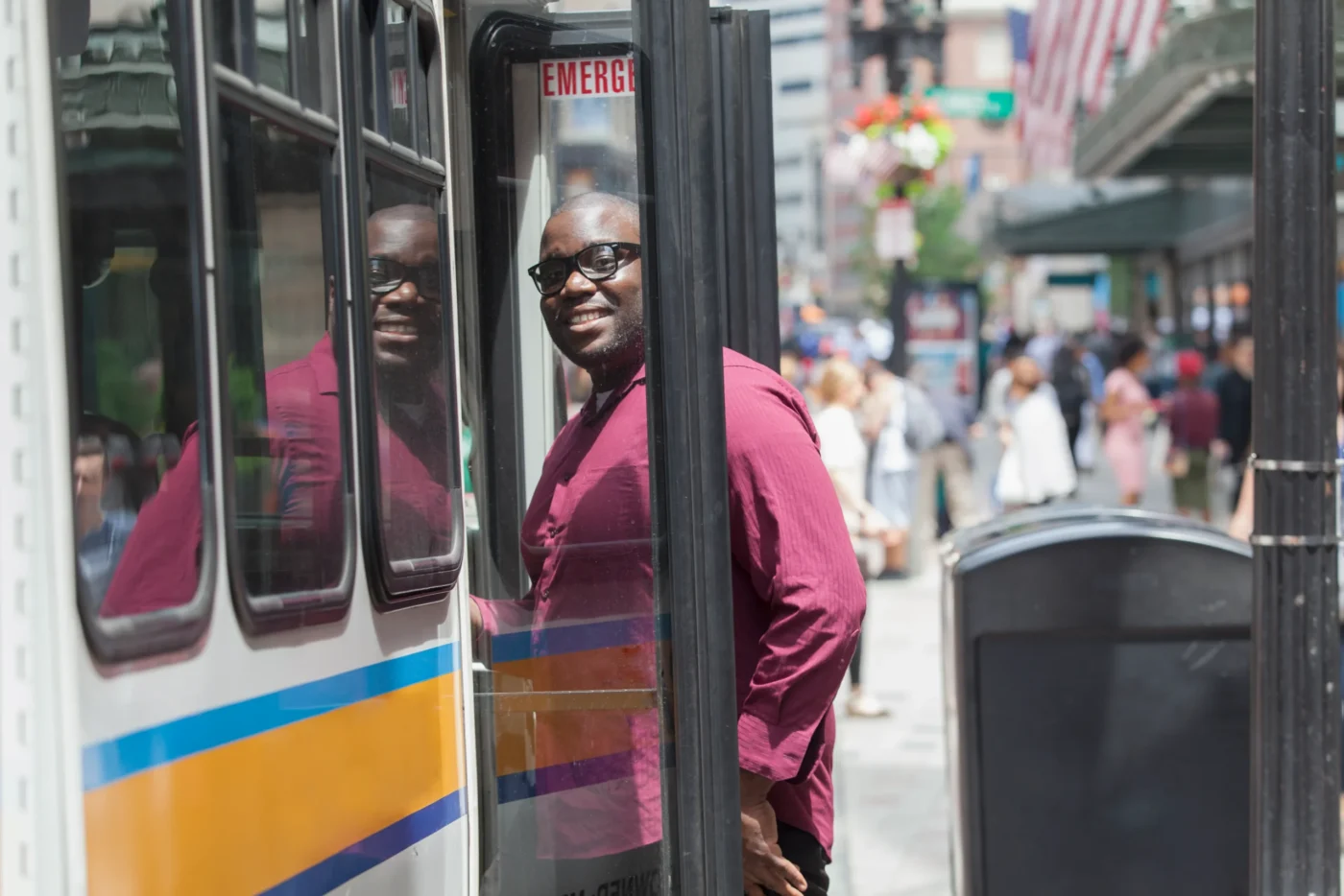 Man boarding a bus and smiling at the camera, wearing casual clothes.