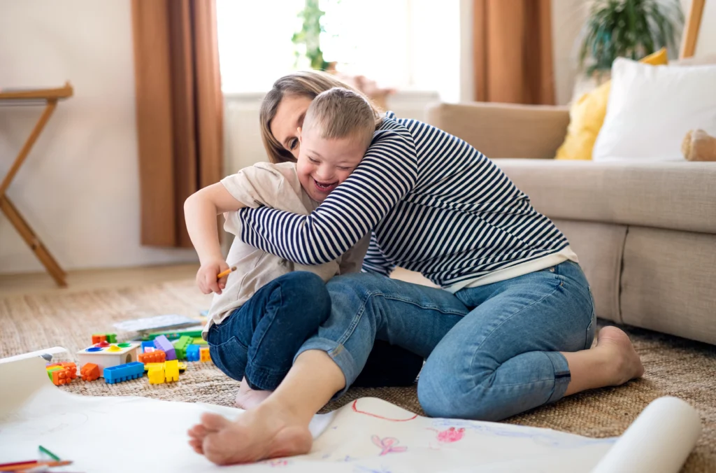 Parent sitting on the floor hugging their child while playing with colorful building blocks in a cozy living room