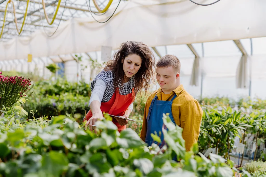 A woman shows a young man a tray of green produce in a greenhouse.